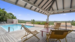 Un espacio al aire libre techado con piscina, sillas de descanso y una mesa.