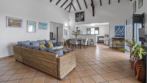 Amplia sala de estar con un sofá de mimbre, una mesa de comedor y una cocina al fondo.