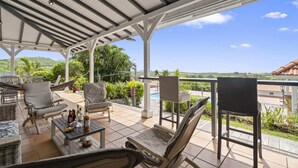 Un espacio de estar al aire libre cubierto con sillas y una mesa, con vistas a una piscina y follaje.