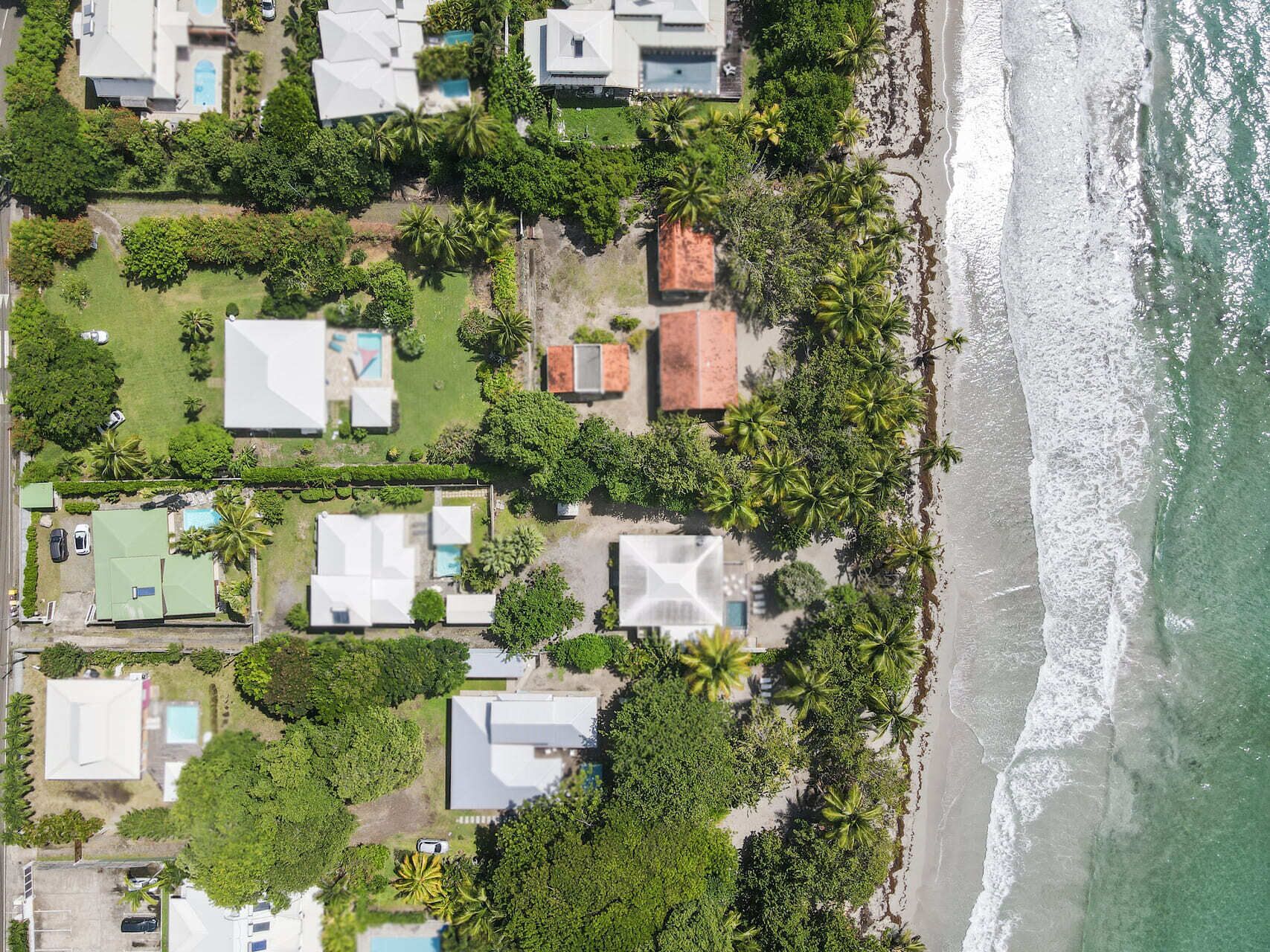 Vista aérea de una zona residencial costera con casas, una playa y una piscina.