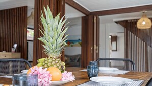 Una mesa de comedor con una piña, una naranja, flores rosadas y un vaso de agua.