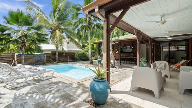 Un área de piscina con sillones de descanso, una zona de estar cubierta y un gran jarrón decorativo.