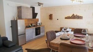 Een moderne woonkamer met een bank, een eettafel met stoelen en een keuken met kasten en apparatuur.