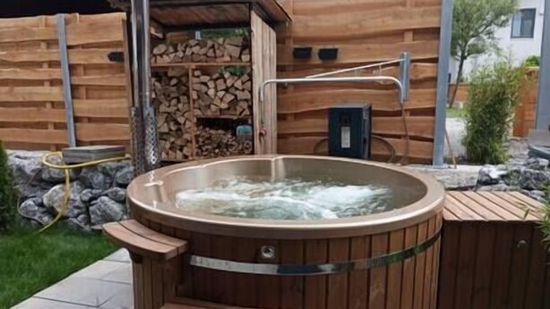 Een hottub met een houten buitenkant, omgeven door een houten terras en een stenen muur.