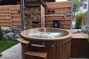 Ein Whirlpool mit Holzverkleidung, umgeben von einer Holzterrasse und einer Steinmauer.