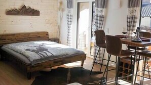Een slaapkamer met een houten bed, een eettafel met stoelen en uitzicht naar buiten door een raam.