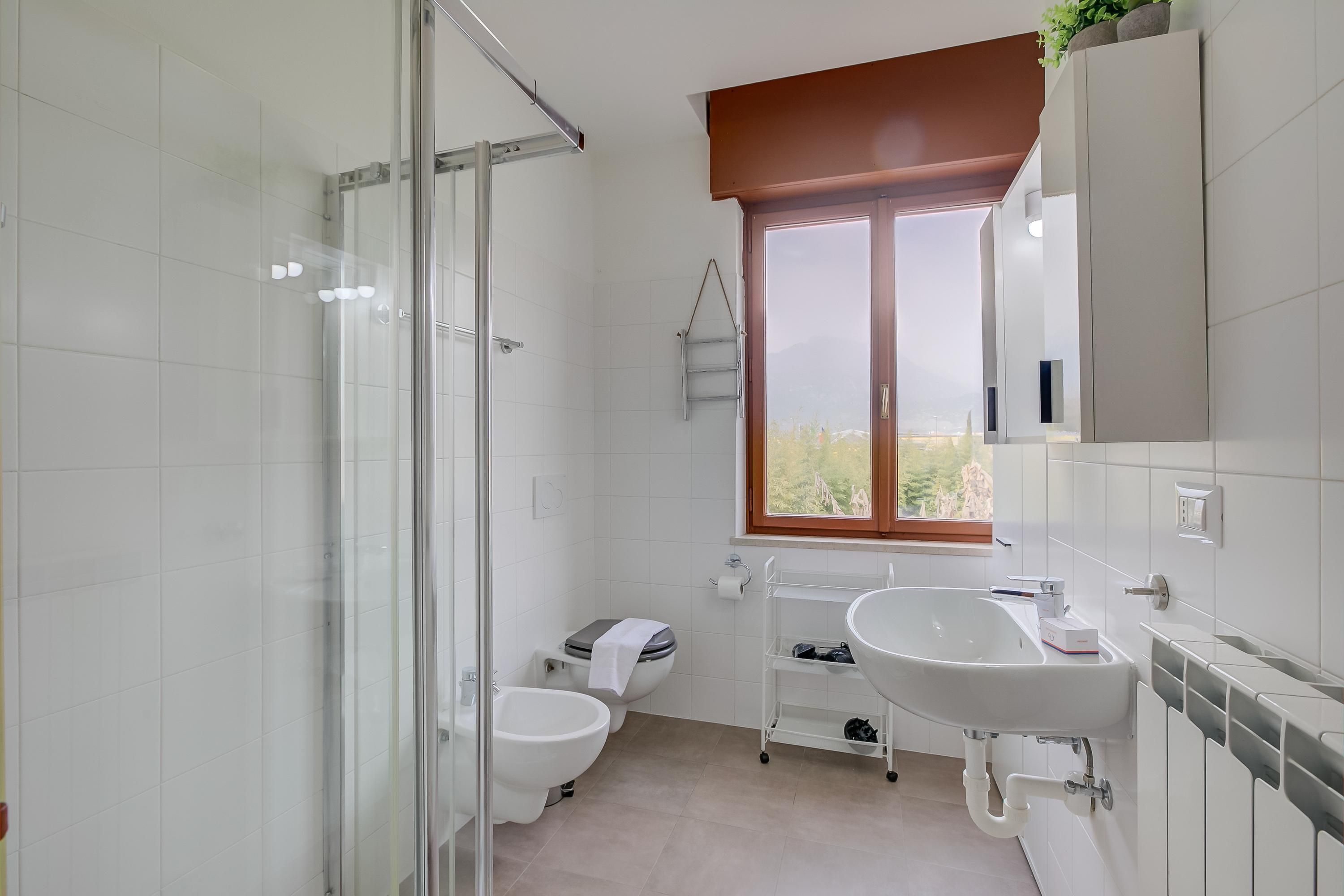 Un baño moderno con cabina de ducha de vidrio, un bidé, inodoro, lavamanos y ventana con vistas.