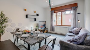 Un soggiorno moderno con zona pranzo, divano, televisore e finestra con tende.