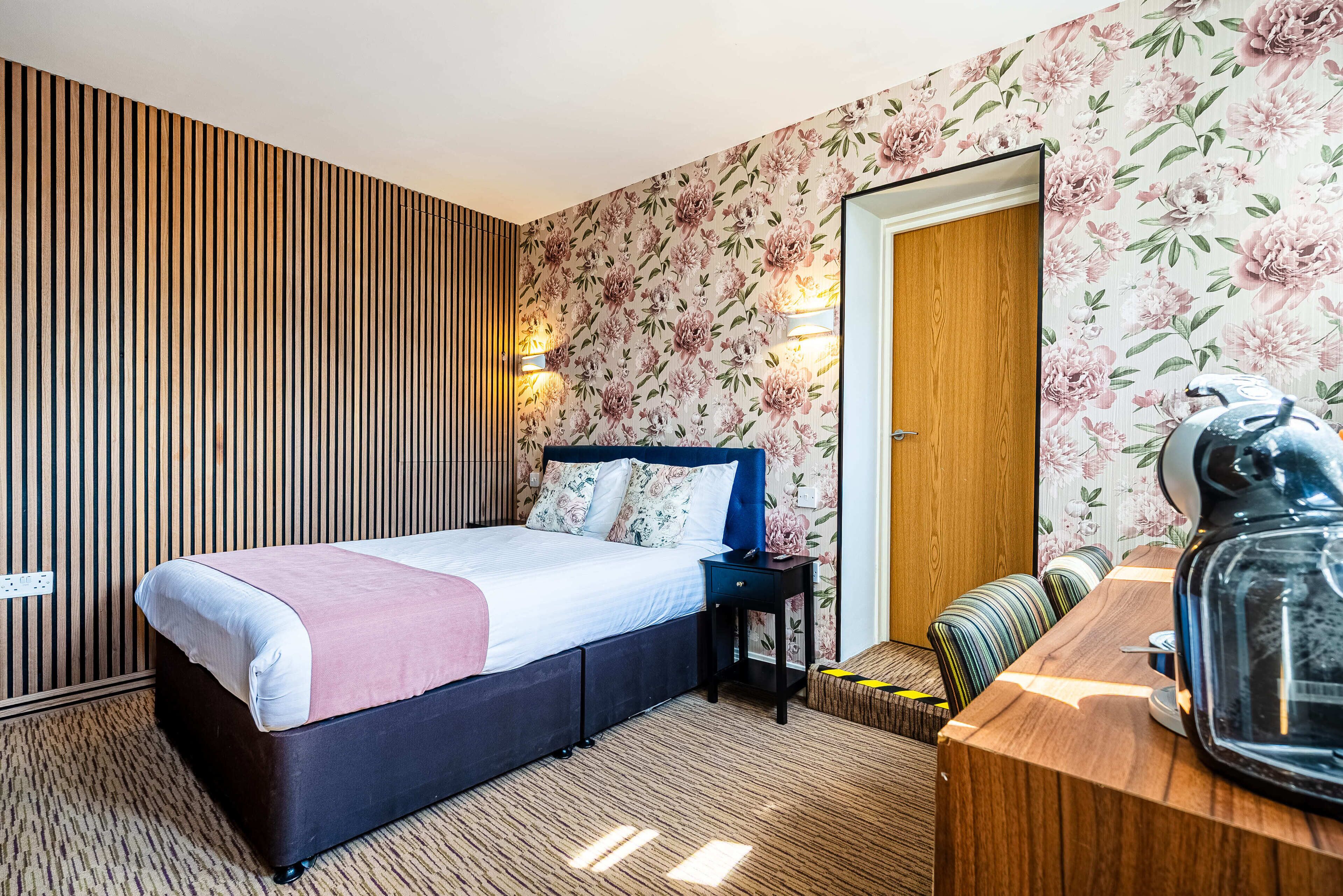 Ett hotellrum med en säng, en byrå i trä, ett litet bord och en spegel.