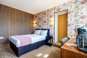 A hotel room with a bed, a wooden sideboard, a small table, and a mirror.