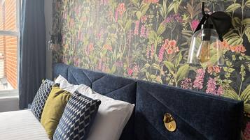 Un dormitorio con cama, almohadillas decorativas, papel tapiz floral y una lámpara colgante.