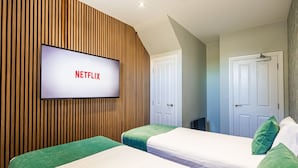 A hotel room with two beds, a wooden wall paneling, a flat-screen TV displaying 'NETFLIX', and two white doors. - Sarah Hotel (Harwich)