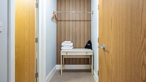 A small, narrow room with a wooden wardrobe, a wooden bench with towels, and a coat rack. - Sarah Hotel (Harwich)