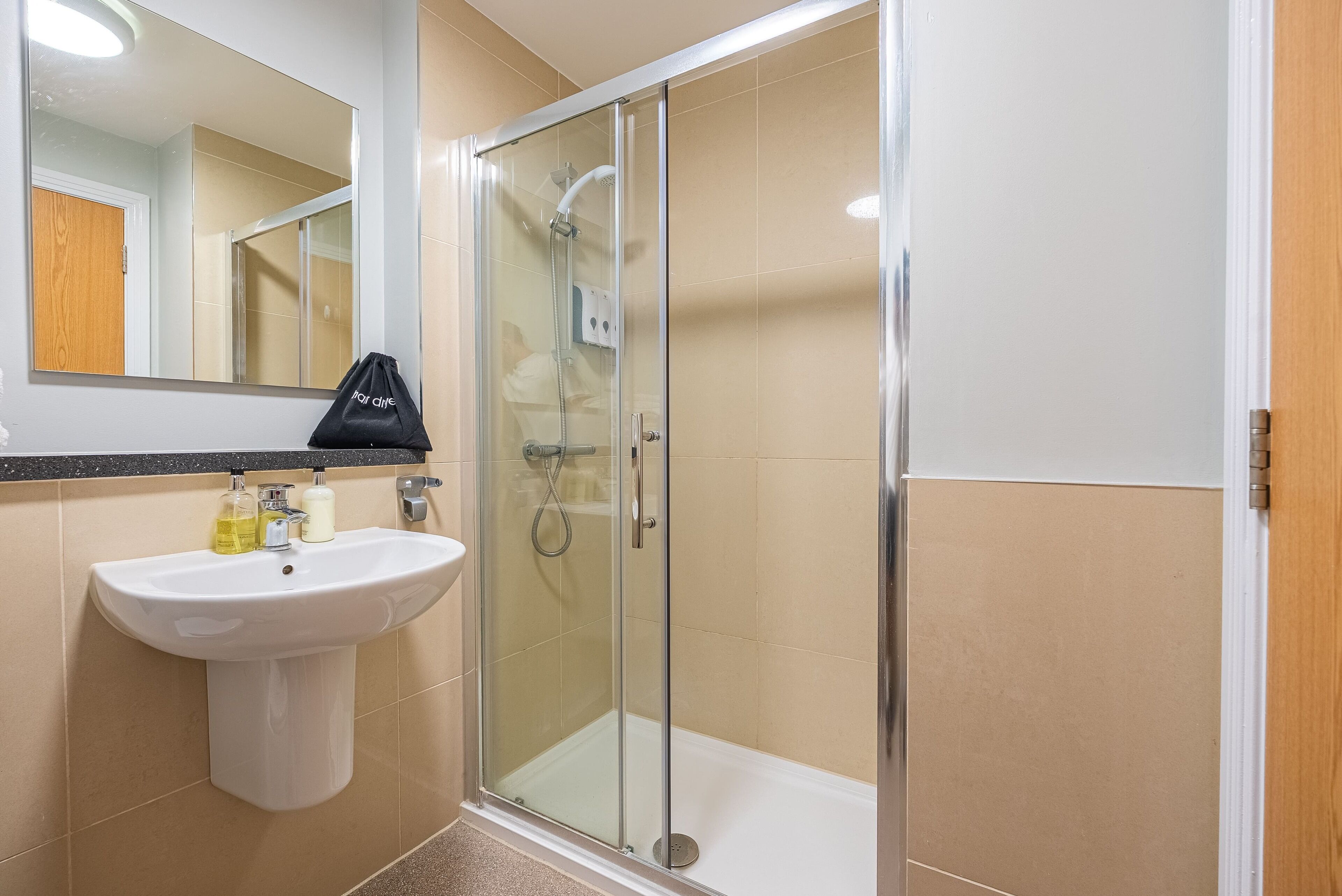A bathroom with a glass-enclosed shower, a sink with toiletries, and a mirror.