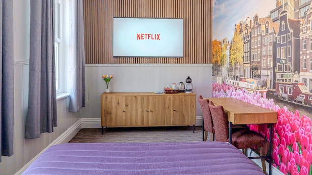 A hotel room with a bed, a wooden cabinet, a desk, and a wall-mounted TV displaying "NETFLIX". - Sarah Hotel (Harwich)