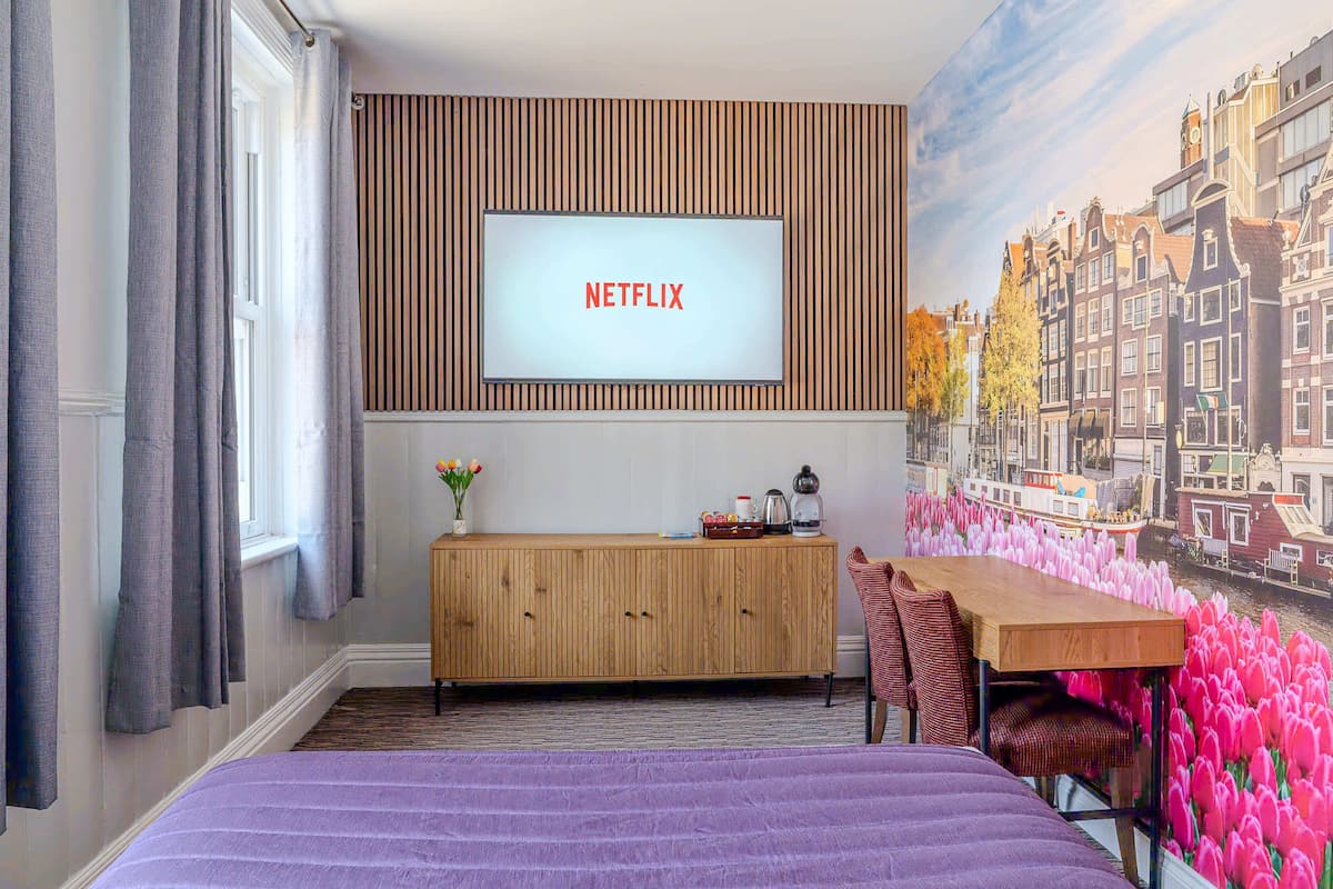 Une chambre d’hôtel avec un lit, une armoire en bois, un bureau et un téléviseur fixé au mur qui affiche « NETFLIX ».