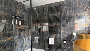 A modern bathroom with a glass-enclosed shower, marble walls, and a black and gold tiled floor. - Sarah Hotel (Harwich)