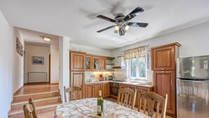A kitchen with wooden cabinets, a stainless steel refrigerator, and a dining table with a wine bottle. - Pool House Robertino (Tar-Vabriga)