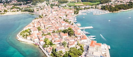 An aerial view of a coastal town with a marina, buildings with red roofs, and clear turquoise waters.