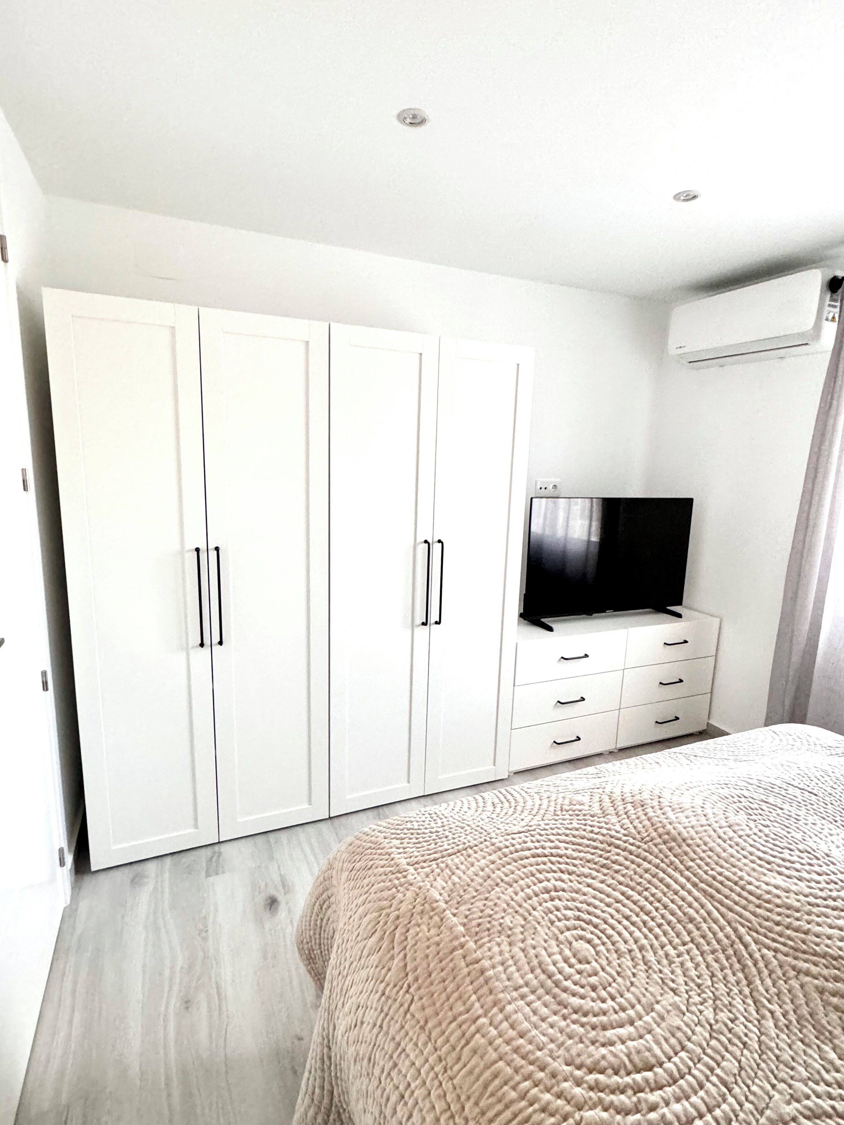 A bedroom with a bed, a TV on a dresser, and white wardrobes.