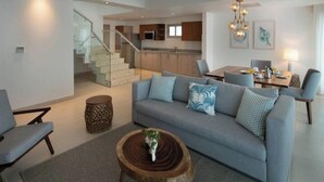 Een moderne woonkamer met een bank, salontafel en een trap naar een keuken.