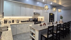Una cucina moderna con mobili bianchi, piani di lavoro in granito e illuminazione a sospensione.