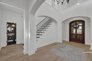 Ein großzügiger Innenraum mit einer Holztreppe, einer großen Holztür und einem gemusterten Teppich auf dem Boden.
