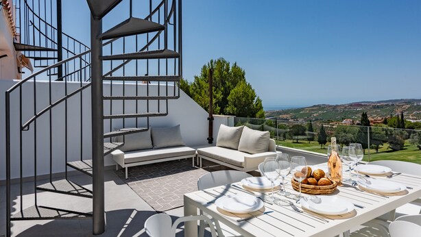 A terrace with a white table set for dining, a sofa, and a spiral staircase. - Hacienda Casares 2053 Geranio (Casares)