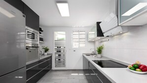 A modern kitchen with stainless steel appliances, a built-in oven, a microwave, a black induction cooktop, and a white countertop. - Hacienda Casares 2053 Geranio (Casares)