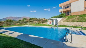 A swimming pool with a lifeguard station, a building with balconies, and a hilly landscape in the background. - Hacienda Casares 2053 Geranio (Casares)