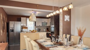Een moderne keuken met roestvrijstalen apparatuur, een eethoek met een houten tafel gedekt voor zes personen, en een keukeneiland met een ingebouwde oven.