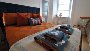 A neatly made bed with a patterned bedspread and two folded towels with a nautical design. - Harbour Haven- idyllic coastal retreat (Anstruther)