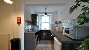 A modern kitchen with a central island, built-in appliances, and a view to the dining area. - Harbour Haven- idyllic coastal retreat (Anstruther)