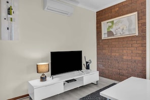 Un soggiorno moderno con una TV a schermo piatto su una console bianca, una lampada e un'opera d'arte incorniciata su un muro in mattoni.