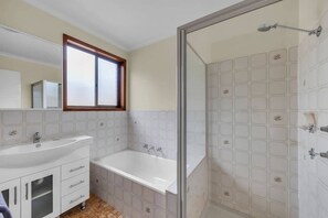 A bathroom with a white sink, a bathtub, and a shower area with a glass door.