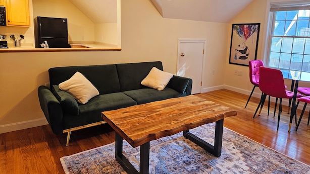 A modern living room with a dark green sofa, a wooden coffee table, and a red chair. - Spacious & Convenient 1BR unit-20min to Boston (Melrose)
