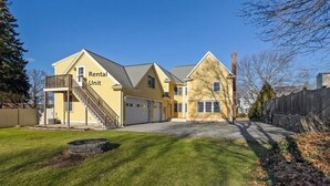 A two-story yellow rental unit with a covered porch, a staircase, and a driveway. - Spacious & Convenient 1BR unit-20min to Boston (Melrose)