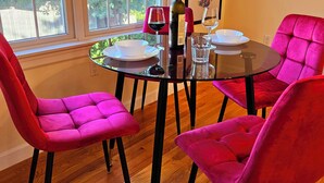 A dining area with a round table, four pink chairs, a bottle of wine, and a painting on the wall. - Spacious & Convenient 1BR unit-20min to Boston (Melrose)