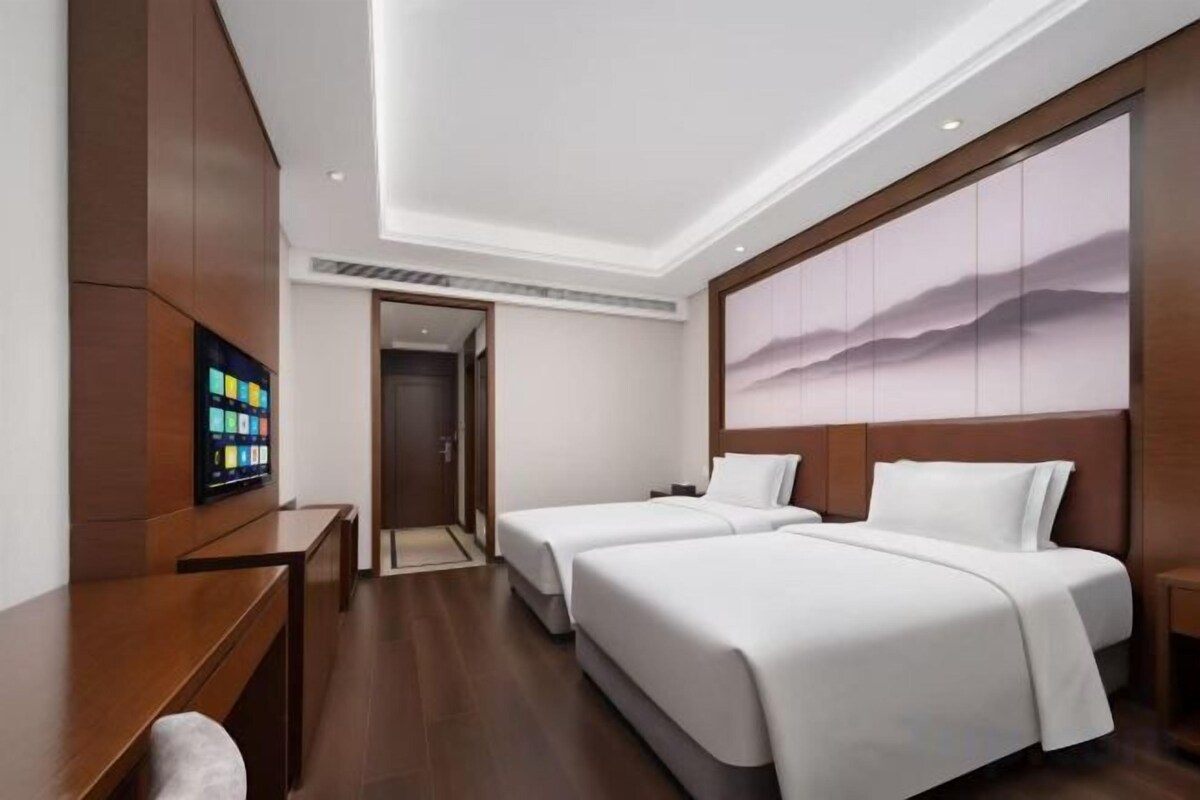 A hotel room with two beds, a desk, a TV, and a large painting on the wall.