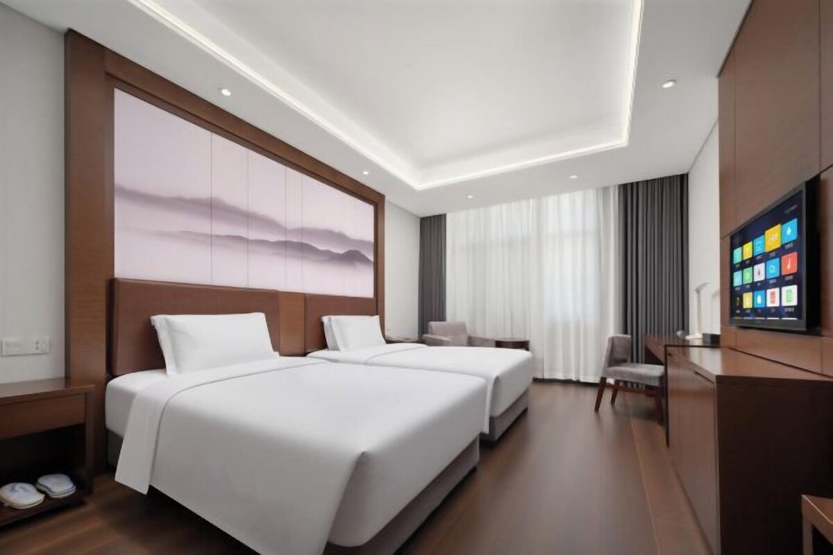 A hotel room with two beds, a TV, a desk, and a large window.