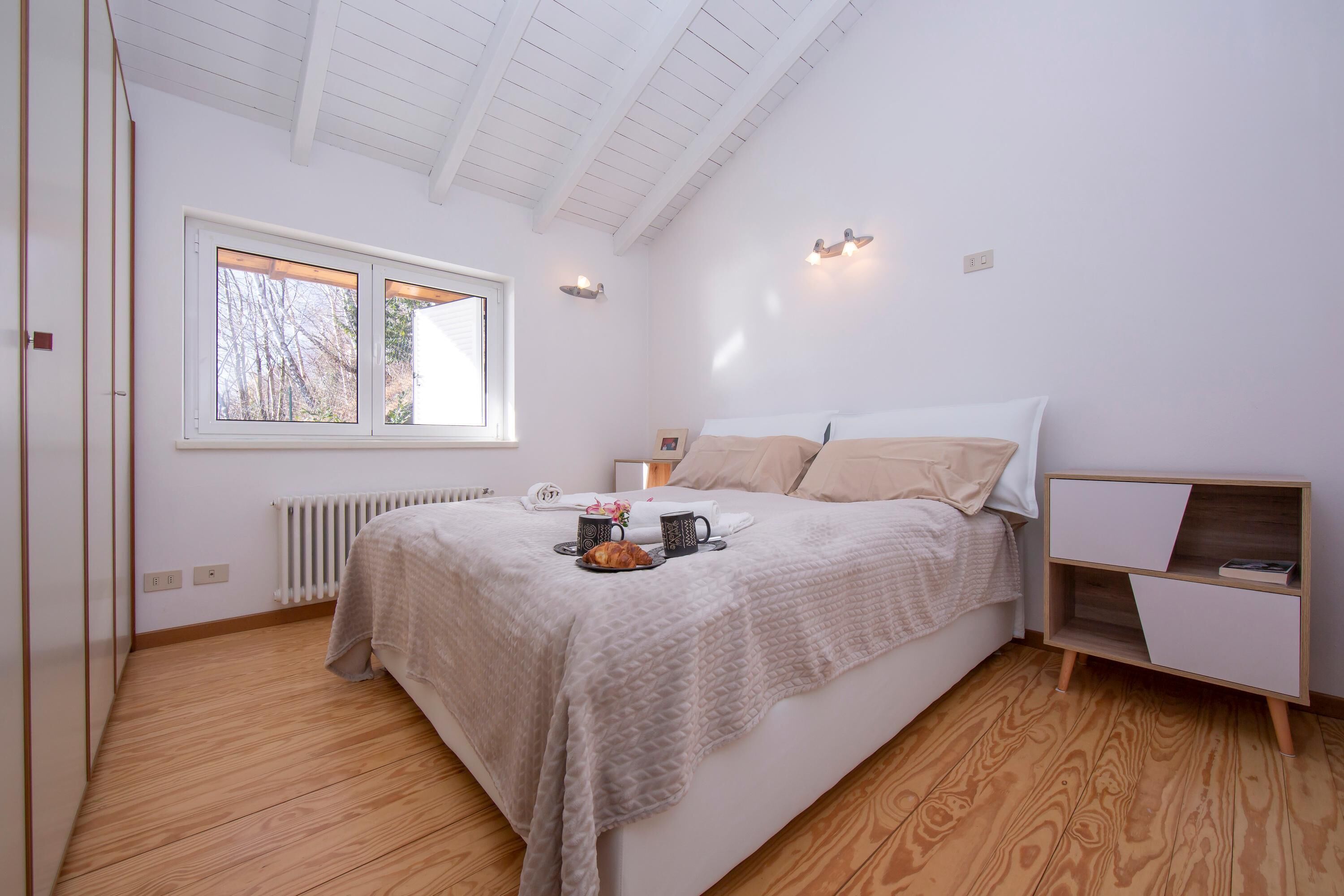 A bedroom with a bed, a nightstand, a window, and a radiator.