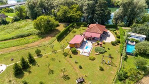 Una casa grande con techo rojo, piscina y jardín bien cuidado.