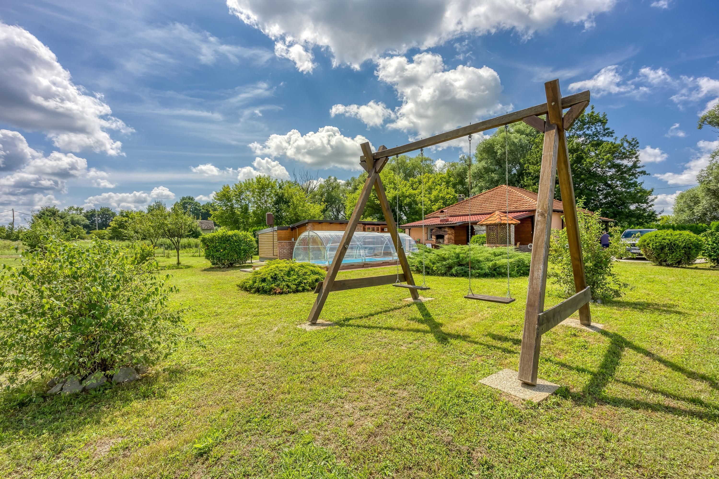 Un ensemble de balançoires en bois installé dans une cour verdoyante, avec une maison en arrière-plan.