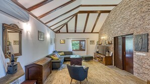Amplia sala de estar con pared de piedra, vigas de madera, un sofá, una mesa de centro y un televisor.