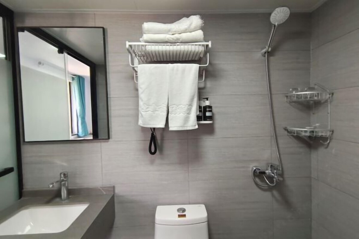 Une salle de bain moderne avec un lavabo, des toilettes et une douche. On y trouve des serviettes sur un porte-serviettes et un miroir au-dessus du lavabo.