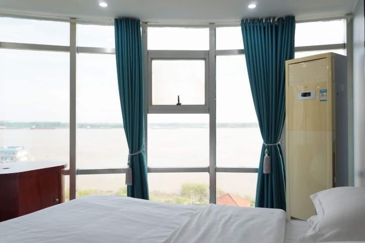 Ein Hotelzimmer mit Bett, Schreibtisch, Kleiderschrank und einem großen Fenster mit Vorhängen.
