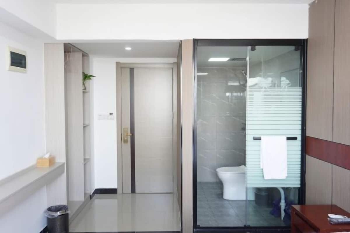 Ein Hotelbad mit Glastrennwand, Toilette, Waschbecken und Mülleimer.