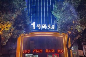 A building with a prominent illuminated sign, a large entrance, and a tree in the foreground. - Anqing No.1 Pier Hotel (Anqing)