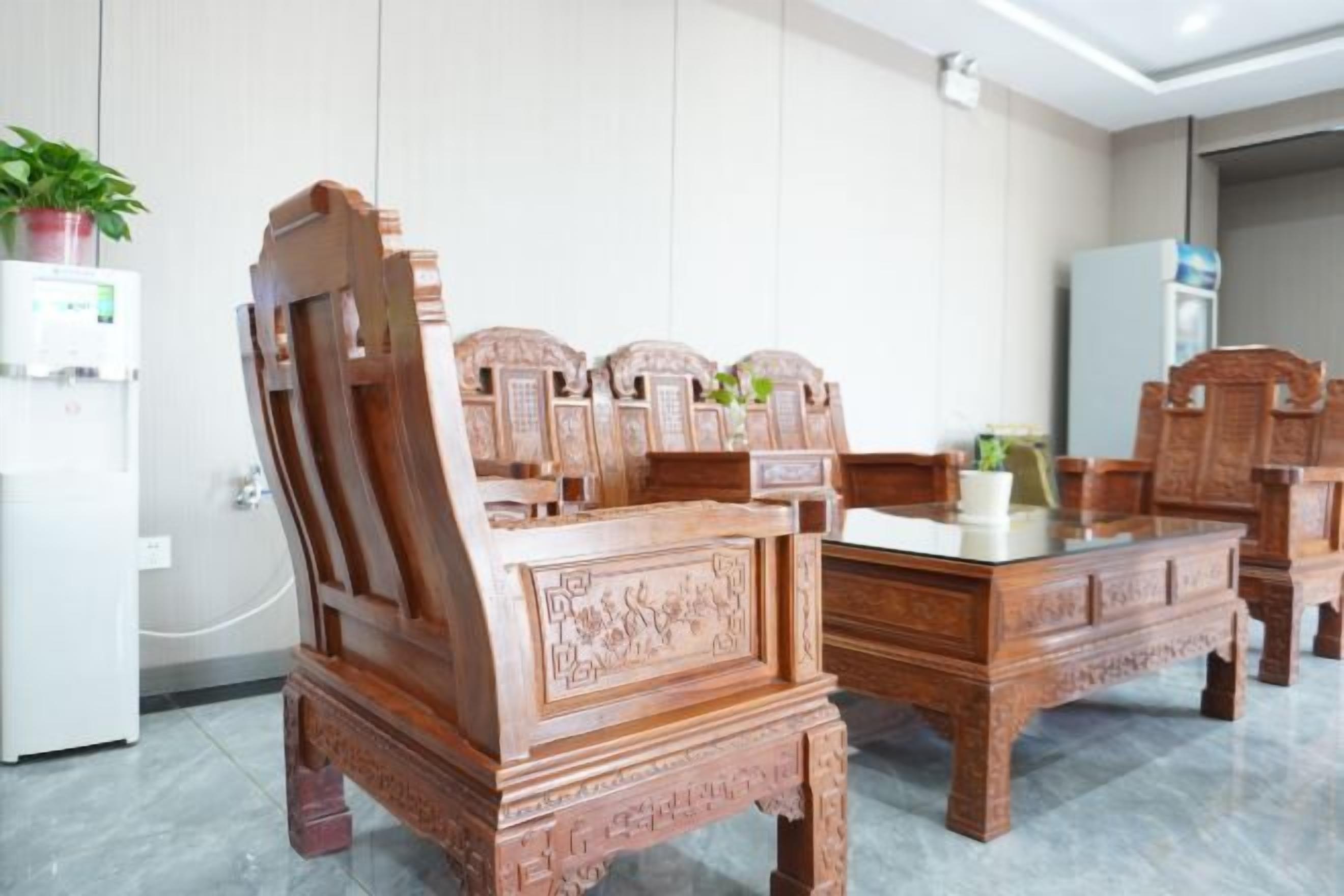 A room with a wooden bed, a desk, and a chair. There is a plant on the wall and a refrigerator in the corner.