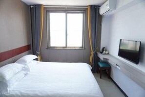 A hotel room with a bed, a television, a window with curtains, and an air conditioning unit.